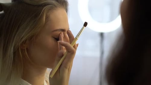 Closeup of Working Makeup Artist Applying Eyeshadow To Eyelids of Young Woman