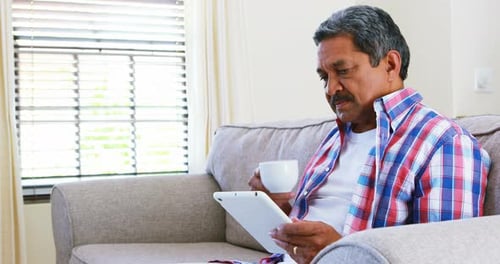 Senior man using digital tablet while having coffee in living room 4k