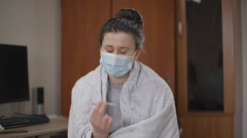 Woman in Mask Holds Thermometer Indoors