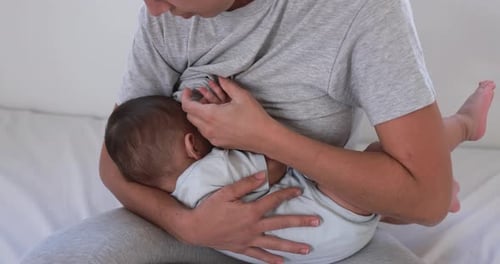 Joven madre amamantando a su bebé en casa sentada en la cama