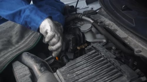 Hand of worker is woman holding oil dipstick checking oil level in engine of car in the garage.