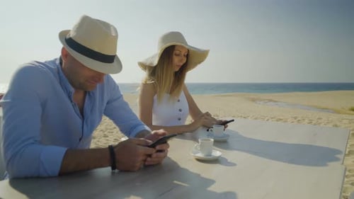 Smiling Couple Using Smartphones on Beach