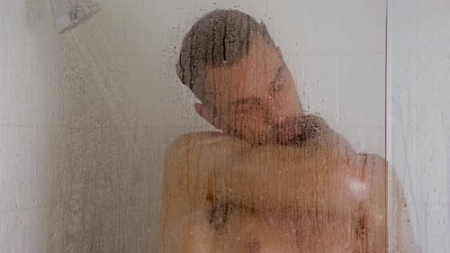 Man taking shower behind glass door