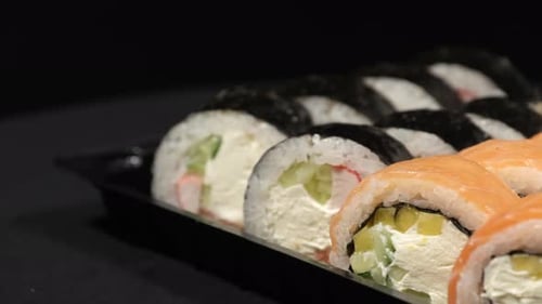 Sushi Rolls Rotates in a Plastic Container on a Black Background. Meal Delivery