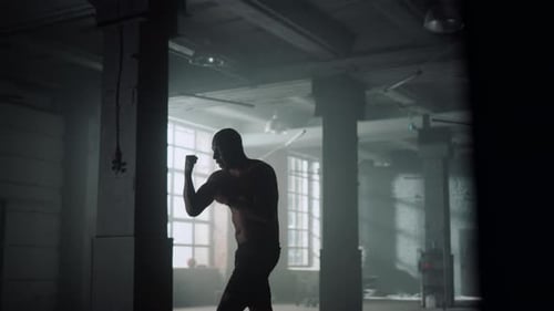 Shirtless Man Boxing Shadow in Dark Gym