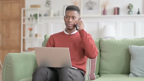 Man Using Laptop, Talking on Phone at Home