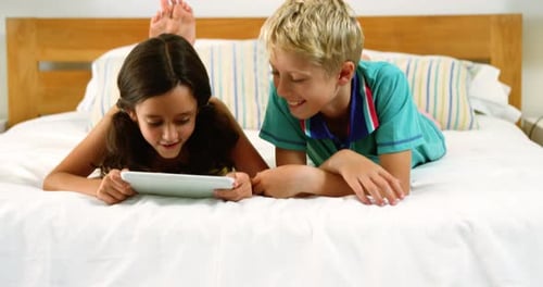 Siblings using digital tablet in bedroom