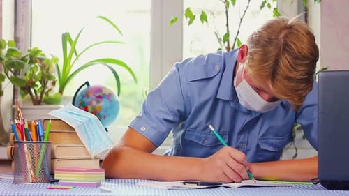 Teenage Student Writes at Desk Wearing Face Mask