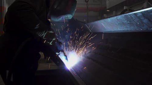 Manuelles Metallschweißen, Funken auf dunklem Hintergrund. Industrielle Produktion. Schutzmaskierter Schweißer