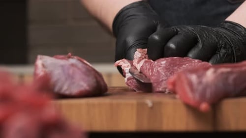 Chef in Restaurant Kitchen Cuts Red Meat or Lamb with Sharp Shiny Knife