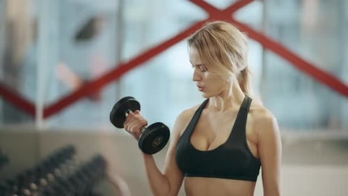 Blonde Female Trainer Doing Dumbbells Exercises in Fitness Gym