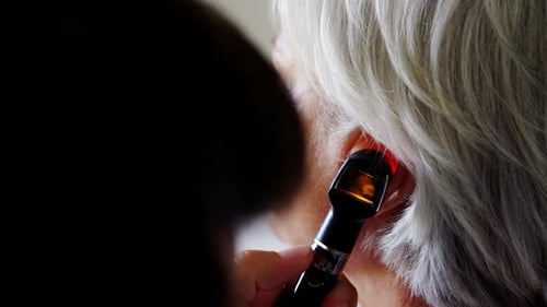 Doctor examining patients ear with otoscope
