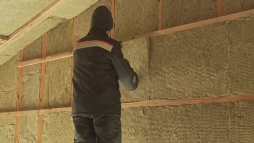 Man Inserts Insulation Between Wood Beams in Attic