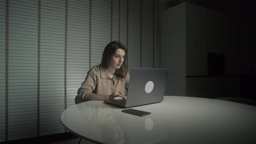 Woman Works on Laptop in Dimly Lit Room