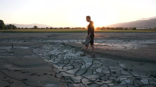 Man Walking Across Cracked Earth at Sunset