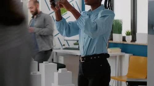 Nahaufnahme einer Frau, die mit Handy arbeitet, um Gebäudemodell und Maquette zu entwerfen