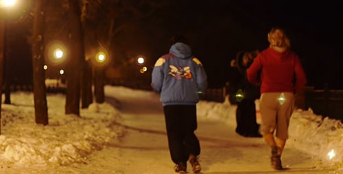 People Walk on Snow Covered Path at Night