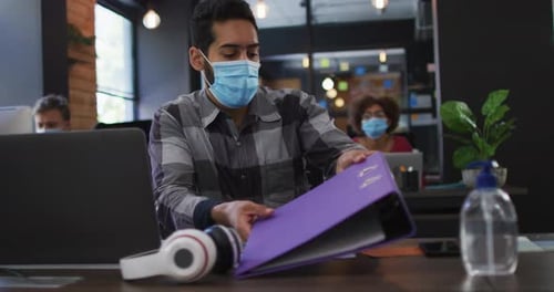 Middle eastern man wearing face mask giving file of documents to his female colleague at modern offi