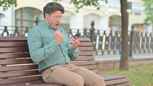 Man Reacts to Content on Cellphone on Bench