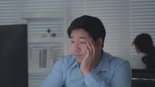 Tired Asian Male Worker Working on desktop computer in the Corporate Office, Work until night