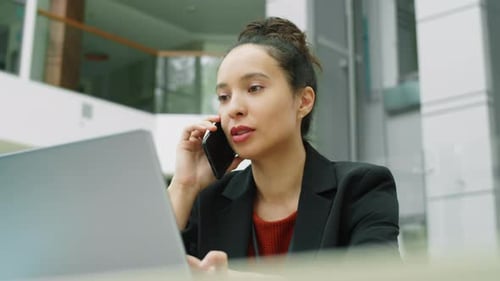Businesswoman Using Laptop and Talking on Phone in Office Center
