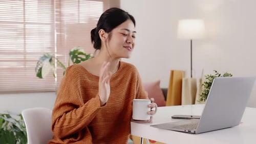 Young modern Asian woman works from home with laptop computer in living room.