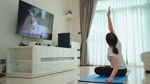 Hermosa joven asiática haciendo ejercicios de yoga, siga las instrucciones del vídeo del entrenador en línea.