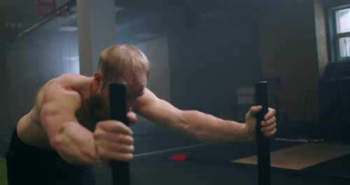 A Powerful Man Pushes a Heavy Weight Trolley in the Gym in Slow Motion. Bearded Man with Vapor on