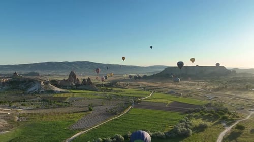 Hot air balloons fly over the mountainous landscape of Cappadocia, Turkey.