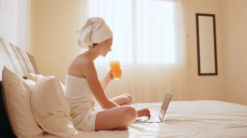 Woman Using Laptop and Drinking Juice in Bedroom