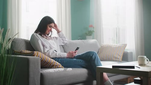 Woman Using Smartphone Leisurely on Gray Couch at Home