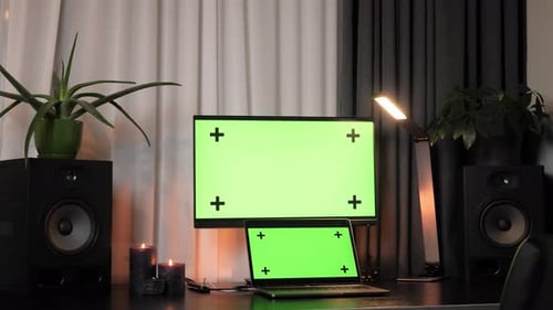 Interior of home office with desk, laptop and computer with mock-up green screen displays.