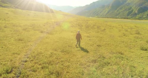 Flight Over Backpack Hiking Tourist Walking Across Green Mountain Field. Huge Rural Valley at Summer