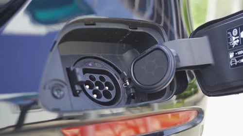 Hand plugging in EV car charger or electric vehicle. Cable connect to gas station