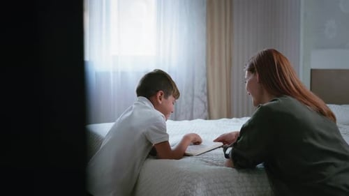 Boy and Woman Reading Book on Bed