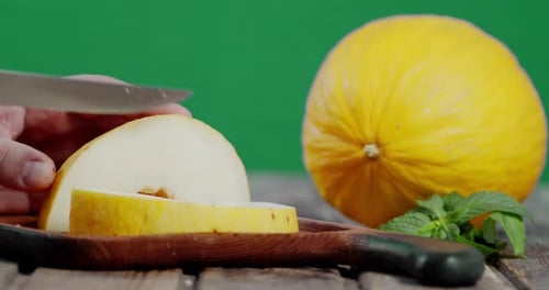 Herb Men coupe un melon en morceaux sur une planche à découper en bois.