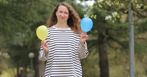 Woman Holding Blue and Yellow Balloons in Park