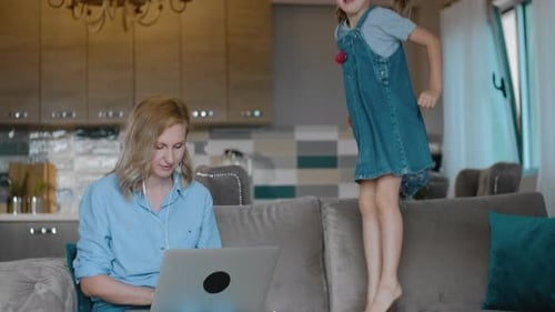 Multitasking-Mutter beim Surfen im Internet arbeitet, während die freudige Tochter auf dem Sofa springt Rbbro