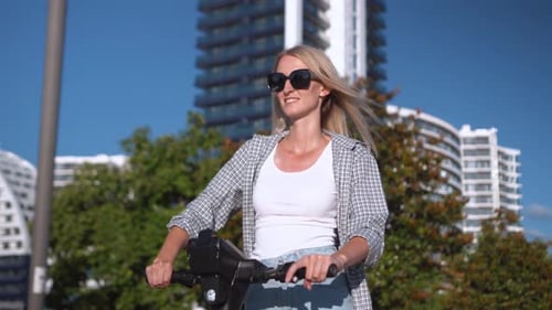 Junges schönes Mädchen fährt im Sommer Elektroroller die Straße entlang,