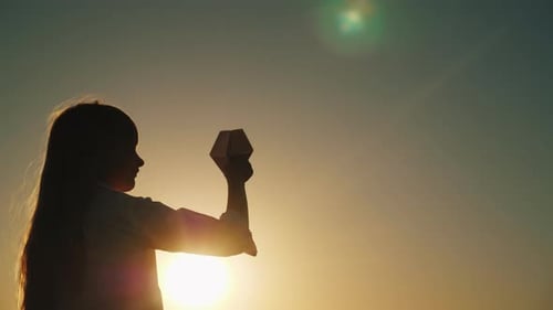 Child Holds Paper Airplane at Golden Sunset