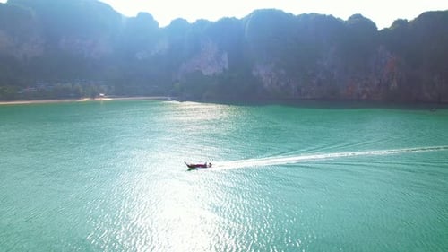4K aerial view over a ship sailing at sea, mountains in the background.