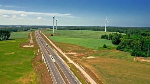 Aerial view of golden field and wind turbines near highway.