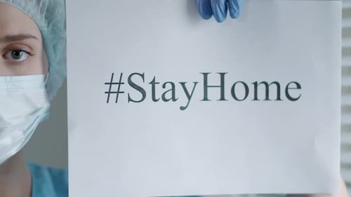 Woman Wearing Mask Holds Stay Home Sign