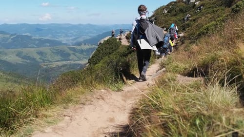 Group of Tourists and Children with Backpacks Go Down on Stone Trail in Mountain