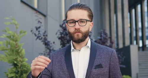 gerente de oficina con gafas y un elegante traje que posa ante la cámara cerca de una oficina moderna