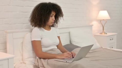 Drowsy Young African Woman with Laptop Falling Asleep in Bed