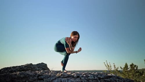 Woman Practicing in Garudasana Eagle Pose Yoga on High Mountain Above Water