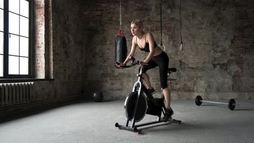 The woman in sport clothes is working out on the exercise bike in the green gym.