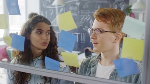 Creative Millennials Arranging Sticky Notes on Glass Wall in Office