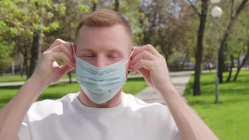 Young Man Putting on Face Mask Outdoors